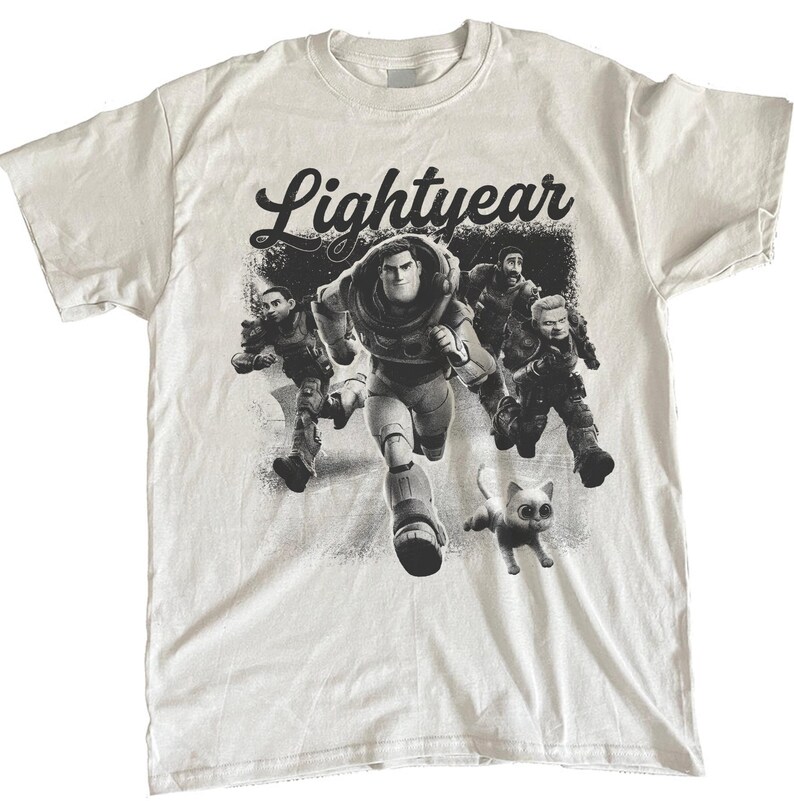 May include: White t-shirt featuring a black and white graphic of characters from the movie "Lightyear." The design includes the word "Lightyear" in a stylized font above a running Buzz Lightyear and other characters, with a small cat.