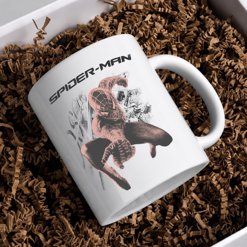 Puede incluir: Una taza de cer&aacute;mica blanca con un gr&aacute;fico negro del personaje Spider-Man en una pose agachada con un gesto de mano lanzando telara&ntilde;as. El texto SPIDER-MAN est&aacute; impreso en letras may&uacute;sculas negras sobre la ilustraci&oacute;n del personaje.