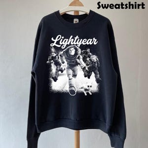 May include: Black sweatshirt featuring a graphic of Buzz Lightyear and other characters from the movie Lightyear. The word "Lightyear" is written in white script above the graphic. The word "Sweatshirt" is written in black block letters at the top.