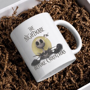 May include: A white ceramic mug featuring a graphic of the character Jack Skellington from The Nightmare Before Christmas. The design includes a yellow moon background, the character in a black suit, and the movie title in black lettering.