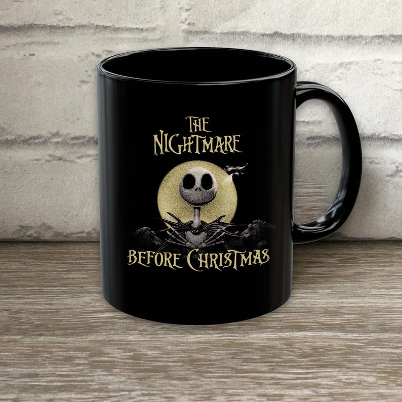 May include: A black ceramic mug featuring a graphic of Jack Skellington from The Nightmare Before Christmas. The design includes a large yellow full moon behind the character, with the text The Nightmare Before Christmas printed in a stylized font.