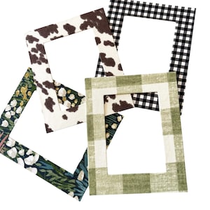 Peut inclure: Plusieurs cadres photo recouverts de tissu aux motifs variés. Les motifs comprennent un imprimé vache, du vichy noir et blanc, du plaid vert et blanc et un motif floral avec des feuilles vertes et blanches et des accents dorés. Les cadres sont carrés avec une ouverture rectangulaire.