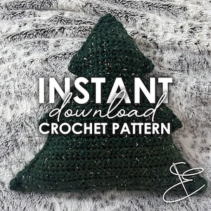 Op de afbeelding: Groen gehaakt kerstboomkussen met de tekst "INSTANT download CROCHET PATTERN" op een witte, pluche achtergrond.