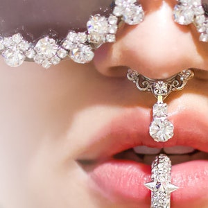 Könnte beinhalten: Nahaufnahme eines Gesichts, das eine silberne Sonnenbrille mit Strasssteinen, einen silbernen Nasenring mit einem baumelnden Strassstein und einen silbernen Lippenring mit Strasssteinen trägt.