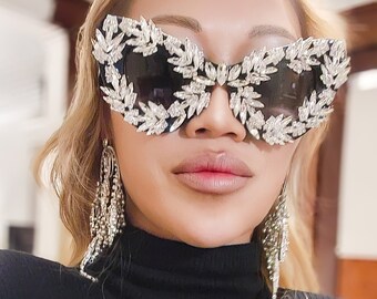 May include: A woman wearing a black turtleneck sweater and large, black sunglasses with rhinestones. The sunglasses have a butterfly shape and are decorated with sparkling crystals.
