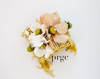 May include: A gold bracelet with a floral design. The bracelet is adorned with rhinestones and features a cluster of white and peach-colored flowers.