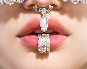 May include: Close-up of a person's face wearing a pair of rhinestone-encrusted sunglasses and a nose ring with a large diamond pendant. The person is also wearing a ring with multiple bands of diamonds on their lower lip.