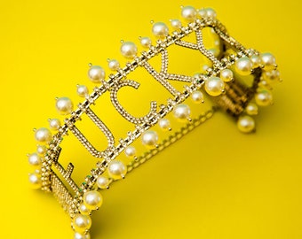 May include: A gold-tone choker necklace with the word "LUCKY" spelled out in rhinestones and accented with white pearls.