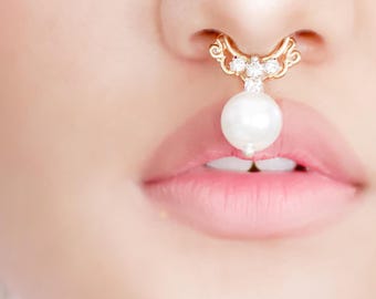 May include: A gold nose ring with a pearl and rhinestones. The ring is worn on a person's nose.