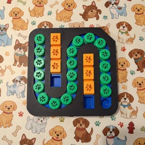 Könnte beinhalten: Ein Hunde-Puzzle-Spiel mit schwarzem Rahmen, mit grünen und orangefarbenen Teilen. Das Spielbrett hat eine U-förmige Bahn mit Pfotenabdruck-Details. Der Hintergrund ist ein cremefarbener Stoff mit verschiedenen Hunde-Illustrationen.