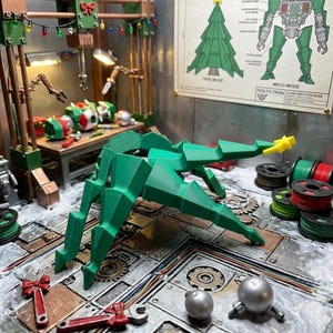 May include: A green, multi-jointed, geometric Christmas tree figure with a yellow star topper. The figure is displayed in a workshop setting with a FES-TV-TRON poster on the wall, featuring a tree mode and a robot mech mode diagram.