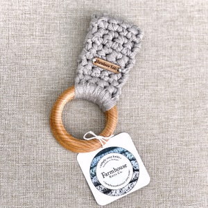 May include: A grey crocheted teether attached to a wooden ring. The teether has a small tag that reads "Farmhouse Knits".