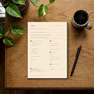 May include: A cream-colored daily planner page with dark text, featuring sections labeled Full day, Scatter, Hours, Top 3, Done Today, Parked - Not Today, and Energy Check-in. The planner is printed on paper with a dark green edge and includes a black pen.