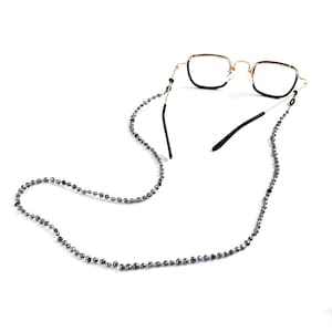 May include: Eyeglasses with a gold frame and black accents, connected to a beaded eyeglass chain. The chain is composed of small, dark gray beads. The glasses have a square shape.
