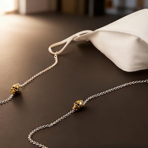 Puede incluir: Una mascarilla blanca con una cadena plateada con detalles de calaveras doradas. La mascarilla est&aacute; hecha de un material suave y transpirable. La cadena est&aacute; dise&ntilde;ada para sujetar la mascarilla alrededor del cuello.