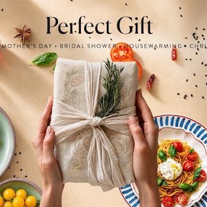 May include: A rectangular package wrapped in beige fabric with a botanical print, tied with a matching fabric strip and a sprig of fresh rosemary. The text Perfect Gift, MOTHER'S DAY, BRIDAL SHOWER, HOUSEWARMING, CHRISTMAS is printed above.
