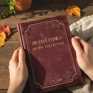 Op de afbeelding: Een bordeauxrode receptenplanner met gouden letters en een decoratieve rand. De omslag luidt "RIVERA FAMILY RECIPE COLLECTION" en "ETS 2026". De woorden "Personalized Recipe Planner" staan bovenaan. De planner wordt door handen vastgehouden.