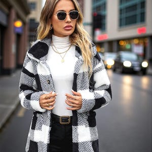 May include: A black and white plaid coat with a button-up front. The coat is worn over a white turtleneck and black pants. The person is wearing sunglasses and gold jewelry. The coat has a classic, oversized fit.