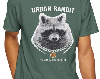 May include: Green t-shirt featuring a detailed illustration of a raccoon wearing a chain necklace. The text "URBAN BANDIT" is above the raccoon, and "TRASH PANDA SOCIETY" is below. The raccoon has a serious expression.
