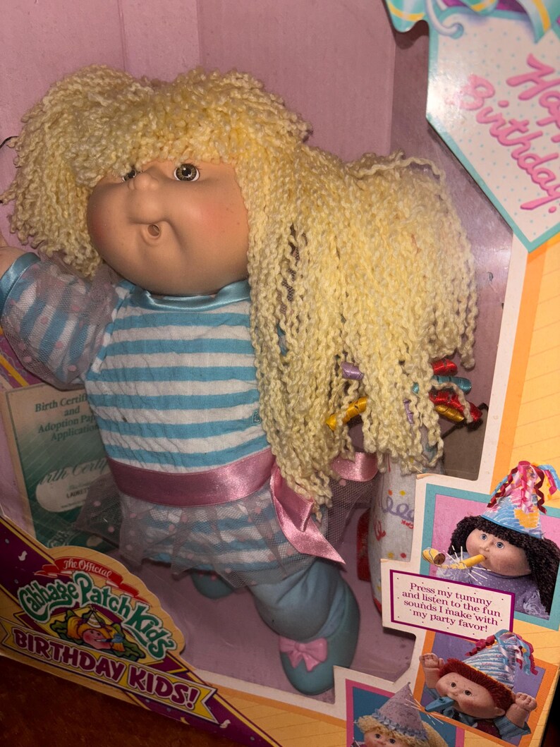 Pu&ograve; includere: Bambola Cabbage Patch Kids Birthday Kids nella sua scatola originale. La bambola ha capelli biondi ricci e indossa un completo a righe blu e bianche con una fascia rosa. La scatola presenta il testo "Happy Birthday" e "Press my tummy and listen to the fun sounds I make with my party favor!"