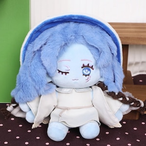 May include: A plush doll with blue skin, blue fluffy hair, and a white dress. The doll has one eye open and one closed, with a small scar detail. The doll is a soft toy.