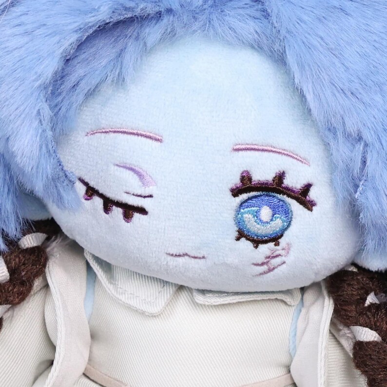 May include: A plush doll with light blue skin, blue hair, and embroidered facial features. The doll has one open eye with a blue iris and brown eyelashes. It wears a white collared shirt and a brown and white patterned accessory.