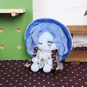 May include: A plush doll with a blue face, hair, and outfit. The doll has closed eyes, a small smile, and brown braids. It is sitting on a black and white polka dot surface.
