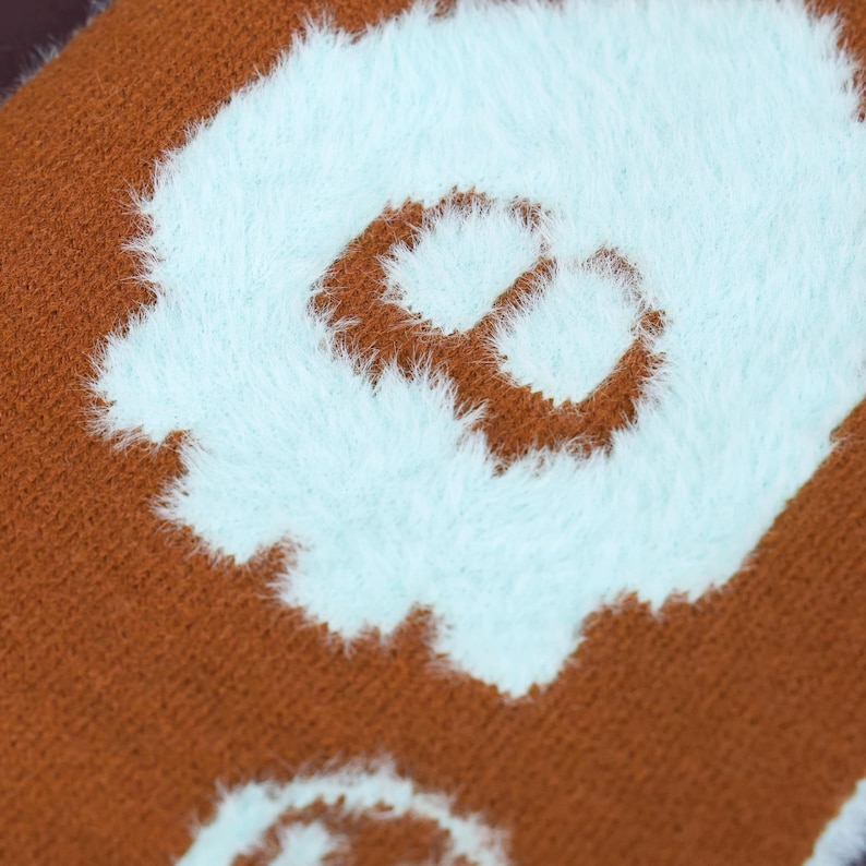 May include: Close-up of a brown textile with a light blue, fluffy, abstract design. The design appears to be a stylized letter or shape. The textile has a soft, textured appearance.