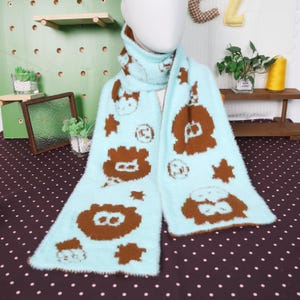 May include: A light blue scarf with brown cartoon animal and star patterns. The scarf is made of a soft, fuzzy material and is draped around a mannequin's neck. The scarf is a winter accessory.