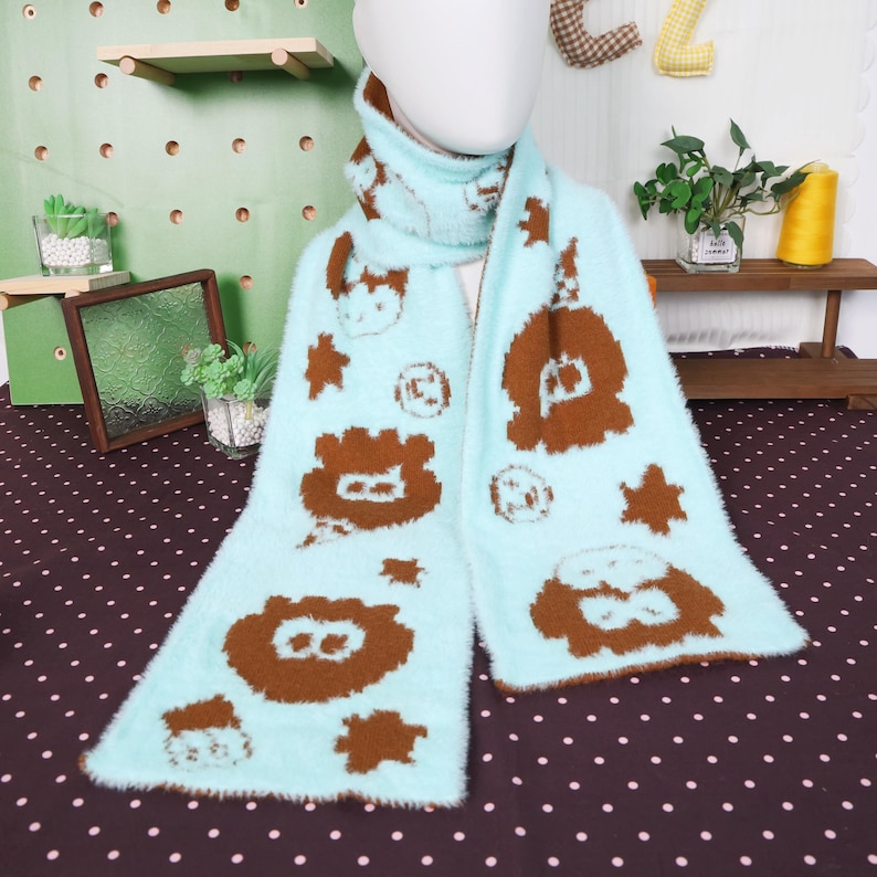 May include: A light blue scarf with brown cartoon animal and star patterns. The scarf is made of a soft, fuzzy material and is draped around a mannequin's neck. The scarf is a winter accessory.