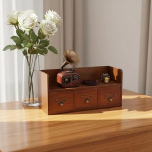 May include: A wooden desk organizer with three drawers and a top shelf. A miniature vintage gramophone and other decorative items sit on the shelf. A vase of white roses is to the left.