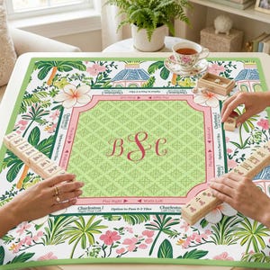 May include: A personalized Mahjong game mat with a green and pink floral design. The mat features a central monogram and is surrounded by tropical flowers and foliage. The game is in progress with tiles and hands visible.