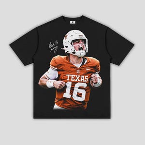May include: A black short-sleeve t-shirt featuring a graphic print of a football player wearing an orange jersey with the text TEXAS and the number 16. The player wears a white helmet and has a signature printed on the upper left side of the chest.