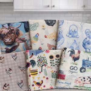 May include: A stack of fabric napkins with various farm animal and rural scene designs. The napkins feature images of chickens, roosters, a Highland cow, and farm-related text. The color palette includes blue, white, pink, and yellow.