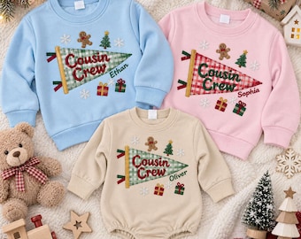 Puede incluir: Una sudadera azul claro, una sudadera rosa y un body beige de manga larga, cada uno con un banderín a cuadros verdes y blancos con el texto Cousin Crew, hombres de jengibre, árboles de Navidad, copos de nieve y cajas de regalo.