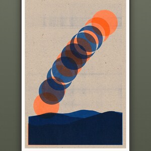 May include: A framed wall art print on textured beige paper featuring a series of overlapping orange and dark blue circles arranged in a diagonal line above a solid dark blue landscape silhouette. The text "MULTIPLE SIZES · INCHES & CM" is visible.
