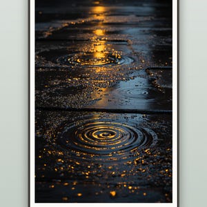 May include: A framed vertical wall art print featuring a dark, wet pavement surface with multiple circular ripples in puddles. The scene is illuminated by golden light reflections, creating a high-contrast effect with deep blue and black shadows.