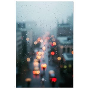 以下が含まれることがあります： 雨の日の街並みを写した写真。雨滴で覆われた窓を通して撮影され、背景にはぼやけた街の建物と街灯があり、ボケ効果でオレンジと赤色の光の円が作られています。