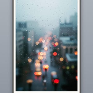 Gouttes de pluie sur une vitre donnant sur une ville floue la nuit, tirage photographique urbain mélancolique