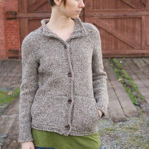 May include: A woman wearing a brown and white knitted cardigan with a green t-shirt underneath and blue jeans.