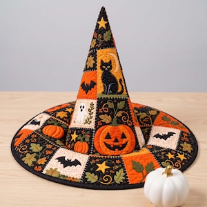 May include: A quilted witch hat featuring a patchwork design with orange, black, and cream fabric squares. The pattern includes embroidered motifs of black cats, jack-o'-lanterns, ghosts, bats, stars, and autumn leaves with visible stitching.