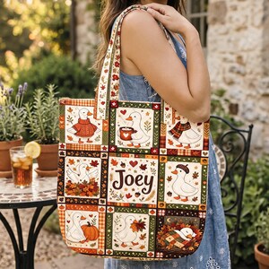 Può includere: Una borsa tote in tessuto rettangolare con un design patchwork di anatre bianche in ambientazioni autunnali. Il motivo include anatre con maglioni, tazze e circondate da foglie autunnali, zucche e ghiande. Il nome Joey è stampato in marrone.