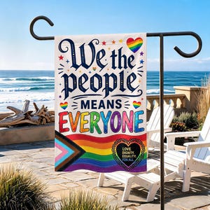 Könnte beinhalten: Eine rechteckige Gartenflagge mit dem Text "We the people MEANS EVERYONE" in dunkelblauer und regenbogenfarbener Schrift. Das Design enthält unten ein Pride-Flaggenmuster, kleine bunte Sterne, Herzen und ein schwarzes Herz mit Text.