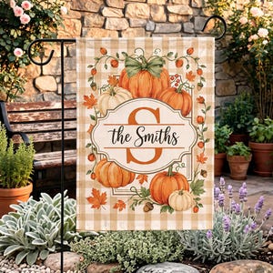Puede incluir: Una bandera de jardín rectangular con un patrón de cuadros beige y blanco. El centro muestra una letra S naranja grande con el texto the Smiths en letra cursiva negra. Está decorada con calabazas naranjas, hojas verdes y bellotas.
