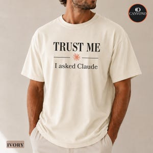 May include: An ivory short-sleeve t-shirt featuring the black text "TRUST ME" above a small coral-colored starburst icon and the black text "I asked Claude" below. The shirt has a crew neckline and a relaxed fit, with a circular logo in the corner.