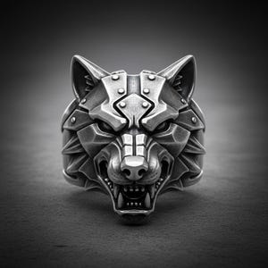 Peut inclure: Bague argentée représentant une tête de loup détaillée. Le visage du loup est finement travaillé avec des dents acérées et une expression féroce. La bague a un style audacieux et géométrique, avec un fond sombre.