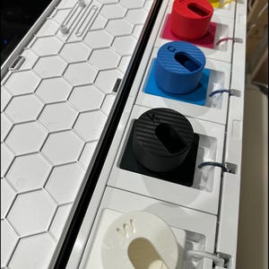 May include: A white mechanical keyboard case with a honeycomb pattern. The case holds several colored keycaps: yellow, red, blue, black, and white. Each keycap has a unique design and color, with a variety of shapes and textures.