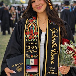 May include: A graduate in a black cap and gown, holding a diploma and a bouquet of red roses. The graduation sash is black with gold trim, floral embroidery, and the text "Gabriella Rivera" and "Class of 2026".