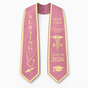 May include: A pink nursing graduation sash with gold lettering and trim. The left side reads "NURSING" with a stethoscope and syringe graphic. The right side includes space for a name, university, RN symbol, and "CLASS OF 2026" with a graduation cap.
