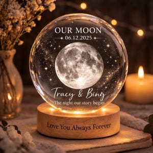 May include: A clear glass sphere with a detailed moon design and embedded stars, resting on a wooden base. The sphere has the text "OUR MOON 06.12.2025" and "Tracy & Bing". The base reads "Love You Always Forever".